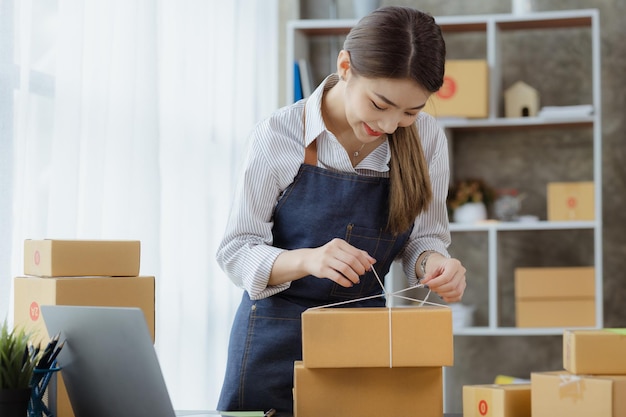 Een Aziatische vrouw bindt een pakket aan de doos van een klant Ze heeft een online winkel die ze inpakt en verzendt via een particulier transportbedrijf Online verkoop en online winkelconcepten