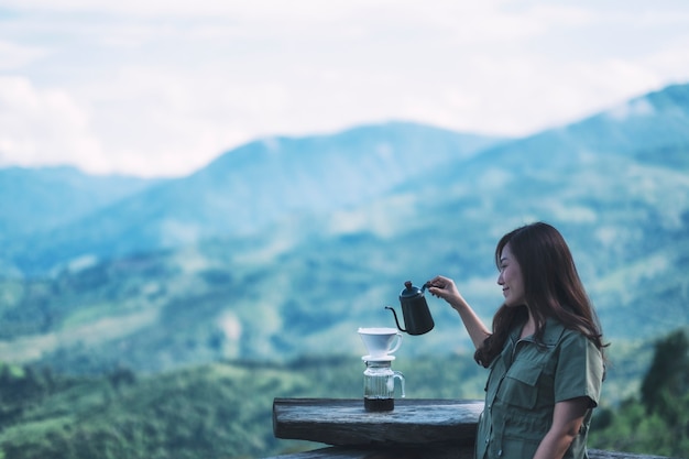 Een aziatische vrouw die infuuskoffie maakt met een prachtige groene berg en de natuur op de achtergrond