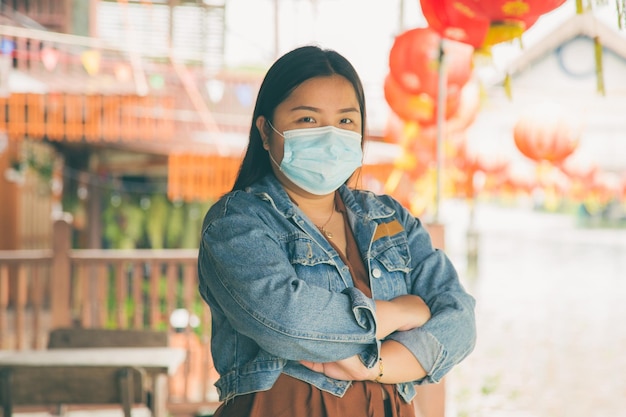 Een Aziatische vrouw in vrijetijdskleding die een masker draagt en haar armen kruist terwijl ze naar een camera kijkt