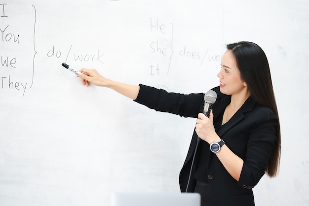 Een Aziatische vrouwelijke lerares van middelbare leeftijd houdt de microfoon vast op het whiteboard van de klas aan de universiteit