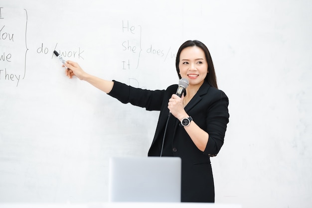 Een Aziatische vrouwelijke lerares van middelbare leeftijd houdt de microfoon vast op het whiteboard van de klas aan de universiteit