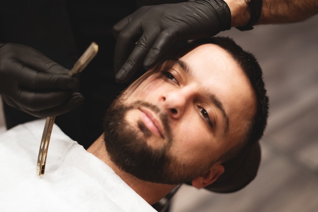 Een baard scheren in kapperszaak met een gevaarlijk scheermes. Kapper winkel baardverzorging. Drogen, knippen, een baard knippen.