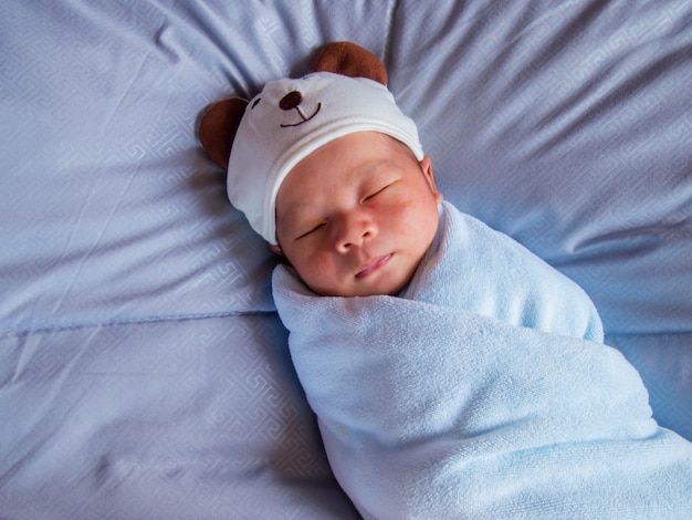 Een baby gewikkeld in een doek en draagt een schattige berenhoed