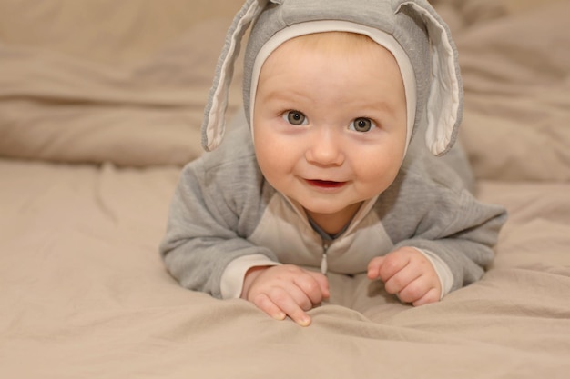 Een baby in een grijze outfit ligt op een bed met een wit laken.