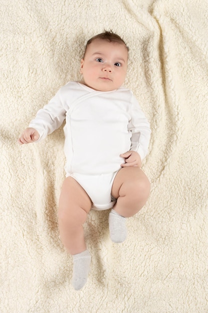 Een baby in een witte bodysuit ligt op een zachte deken Mockup voor ansichtkaarten voor reclameontwerpen