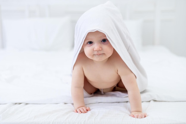 Een baby in een witte handdoek na het baden in een badkuip op een helder bed thuis lacht het concept van hygiëne en wassen