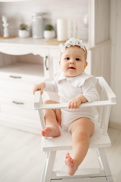 Een baby in een witte katoenen bodysuit zit op een hoge stoel in een helderwitte keuken een kleine lachende babyjongen of -meisje is er babyvoedingconcept