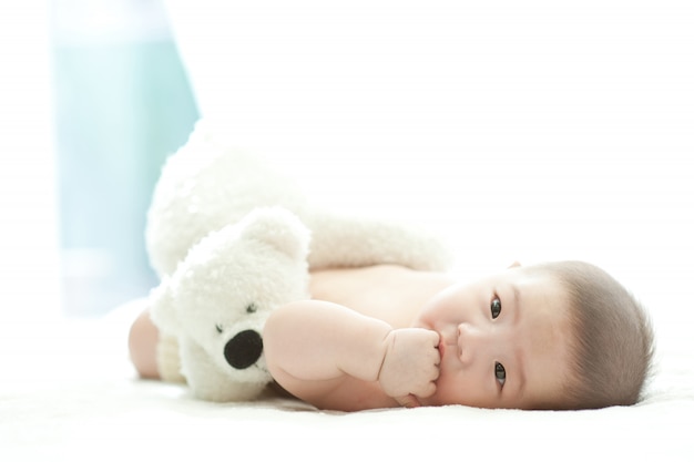 Een baby liggend op een wit bed met een witte achtergrond lacht aan de voorkant.