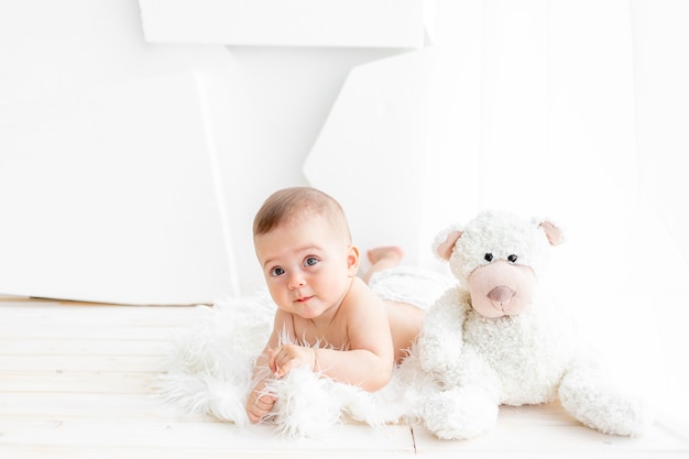 Een baby met een teddybeer ligt in een lichte kamer