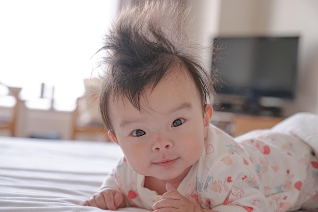 Een baby met veel haar op haar hoofd ligt op een bed.