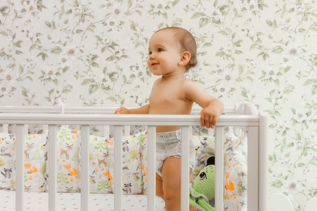 Een baby van 11 maanden in een luier staat in zijn wieg kind in bed