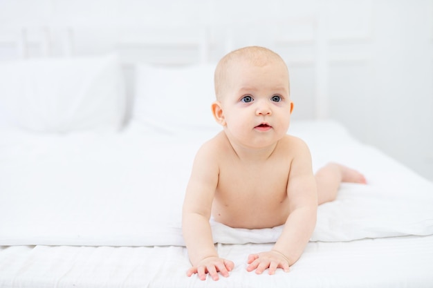 Een baby van zes maanden in luiers op een wit katoenen bed thuis spelend en glimlachend