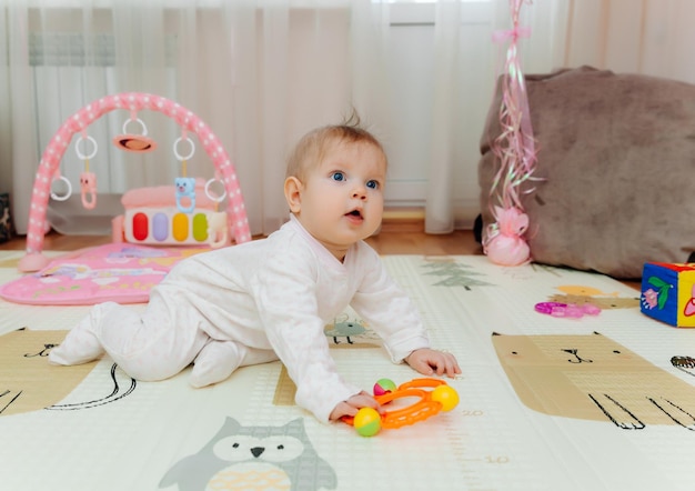 Een baby van zes maanden speelt op de grond met kleurrijk speelgoed. De baby leert portret kruipen