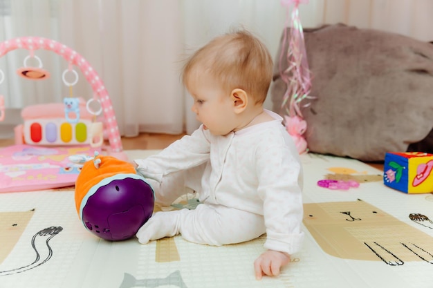 Een baby van zes maanden speelt op de grond met kleurrijk speelgoed De baby leert portret kruipen