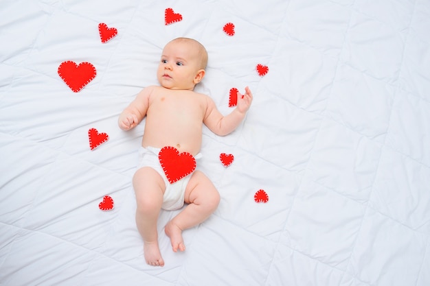 Een babyjongen in een witte luier ligt tegen een achtergrond van rode harten. Liefs, Valentijnsdag