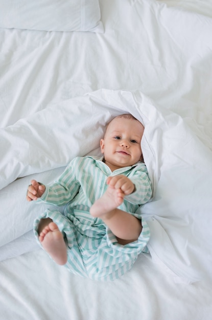 Een babyjongen in gestreepte pyjama ligt op een katoenen deken op het bed en kijkt naar de camera