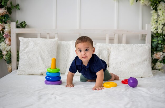 Een babyjongen ligt op handen en voeten op het bed en speelt met een piramidespeelgoed