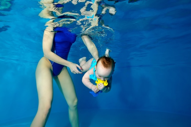 Een babymeisje duikt onder water in een kinderbad met een geel speeltje in haar handen