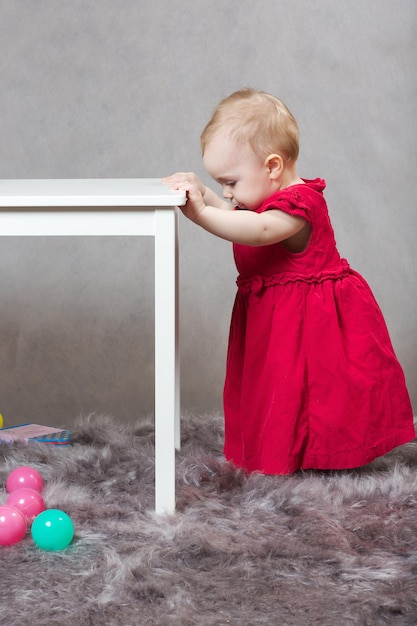 Een babymeisje gekleed in een roodroze fluwelen jurk speelt in de studio