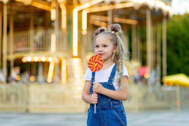 Een babymeisje staat in een pretpark met een grote lolly