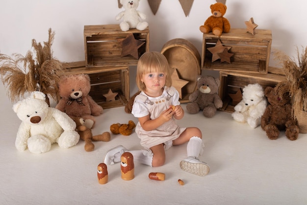 Een babymeisje zit op een witte achtergrond met teddyberen en speelt met een leeuwenwelpje.