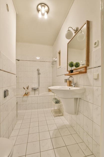 Een badkamer met witte tegels en houten randen rond de badkuip, toilet, wastafel en spiegel aan de muur