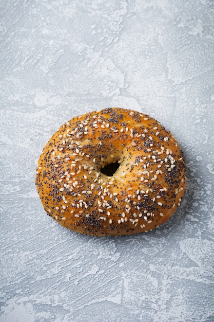 Een bagel met maanzaad en sesamzaad op een grijze steen of betonnen achtergrond