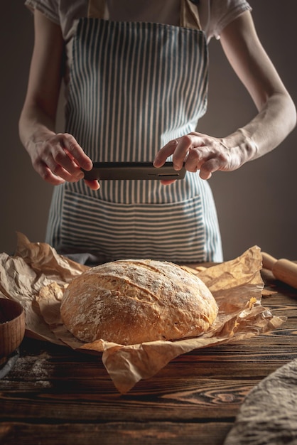 Een bakker maakt foto's van zelfgebakken vers brood op zijn telefoon voor een post op sociale netwerken Bakkerijproducten bakken