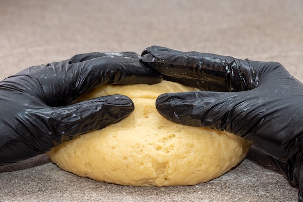 Foto een bal deeg wordt gekneed door een man in zwarte handschoenen. baker's handen kneden deeg met handschoenen op een grijze tafel. thuis taarten, pizza, broodjes maken. thuis bakken concept