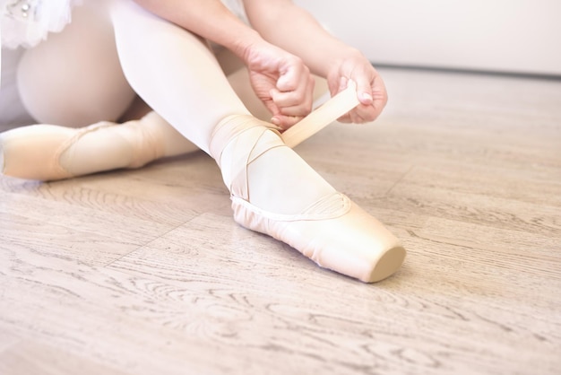 Een ballerina die op de grond zit en haar balletschoenen vastbindt