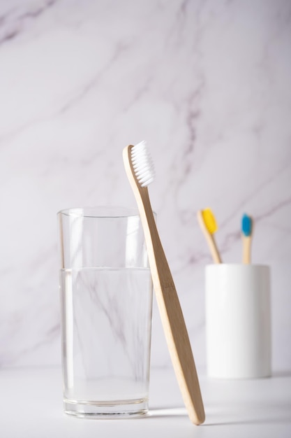 Een bamboe tandenborstel met witte haren naast een glas schoon water