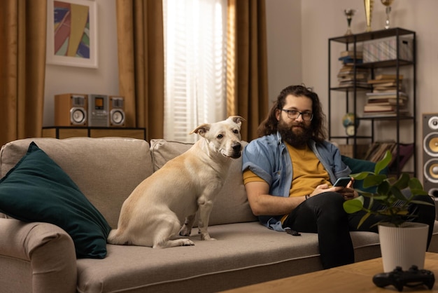 Een bebaarde man brengt zijn vrije tijd door met zijn hond thuis, de jongen houdt een telefoon in zijn handen en