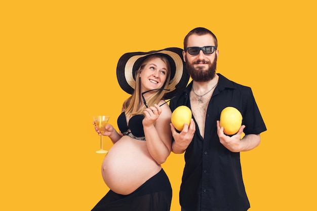 Een bebaarde man en een zwanger meisje in een badpak op een gele achtergrond Verfrissend fruit en drankjes