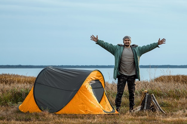 Een bebaarde man in de buurt van een camping tent in oranje natuur en het meer. reizen, toerisme, kamperen.