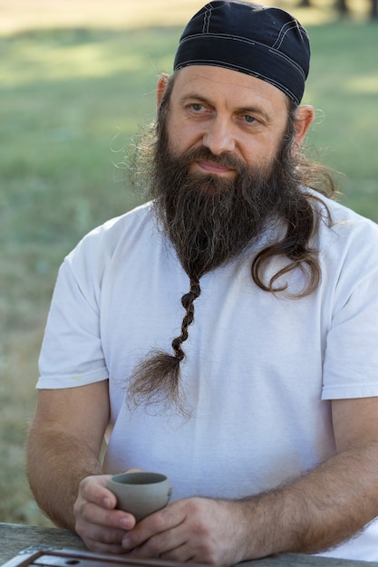 Foto een bebaarde man in een bandana drinkt thee op de achtergrond van de natuur.