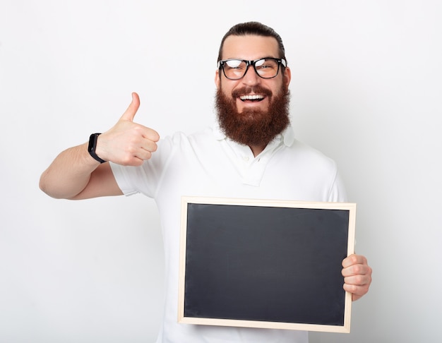 Een bebaarde man met een bril toont duim omhoog en houdt een zwart krijtbord vast.