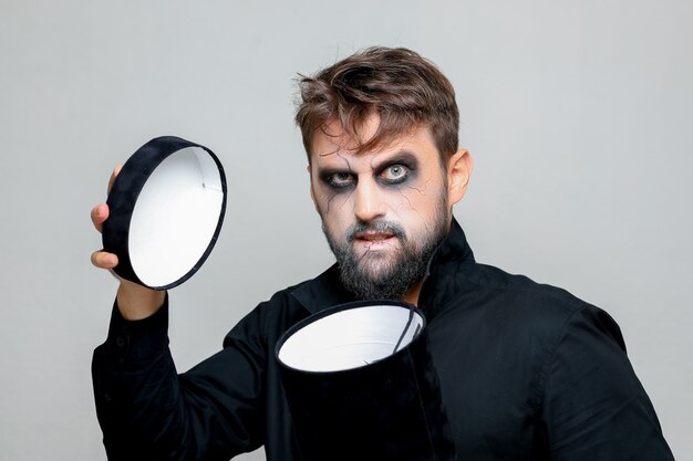 Een bebaarde man met make-up in ondode stijl opent een zwarte doos voor Halloween