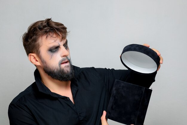 Een bebaarde man met make-up voor Halloween opent een zwarte geschenkdoos