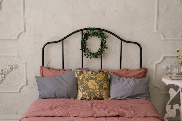 Een bed met roze stoffig beddengoed en grijze kussens in een Scandinavische of klassieke stijl. Op het bed hangt een krans van bladeren