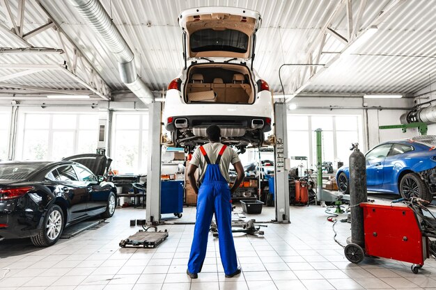 Foto een bedachtzame jonge afrikaanse monteur in een auto-service die naar een auto kijkt en denkt aan een reparatie.