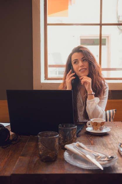 Een bedachtzame vrouw die aan de telefoon belt terwijl ze vanuit een restaurant werkt