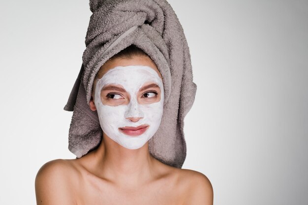 Een bedachtzame vrouw met een handdoek op haar hoofd na een douche zet haar gezichtsmasker op