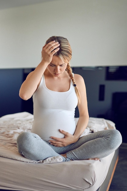 Een bedachtzame zwangere vrouw die thuis op bed zit.