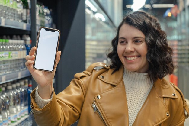 Een beeldschone vrouw met een witte telefoon staat in een supermarkt