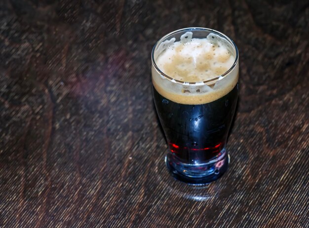 Een beker donker bier schuimt op een houten tafel.