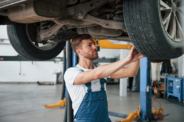 Een bekwame arbeider. werknemer in het blauwgekleurde uniform heeft een baan in de autosalon