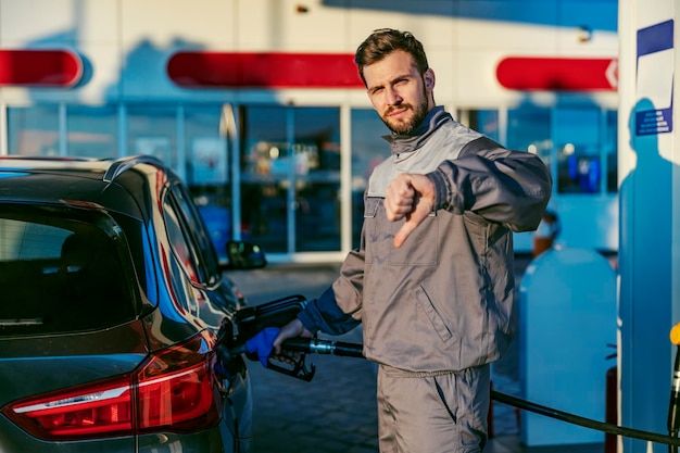 Een benzinestationmedewerker vult de autotank met diesel en geeft duimen naar beneden voor de prijs van diesel