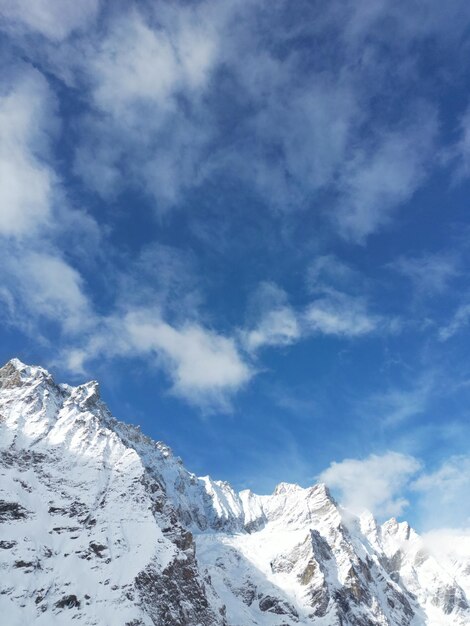 Een bergtop met sneeuw erop en een blauwe lucht met wolken