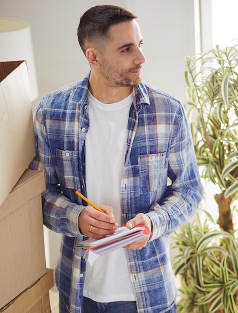 Een bewegende man zittend op de vloer in een leeg appartement Tussen de dozen die de lijst met dingen controleert