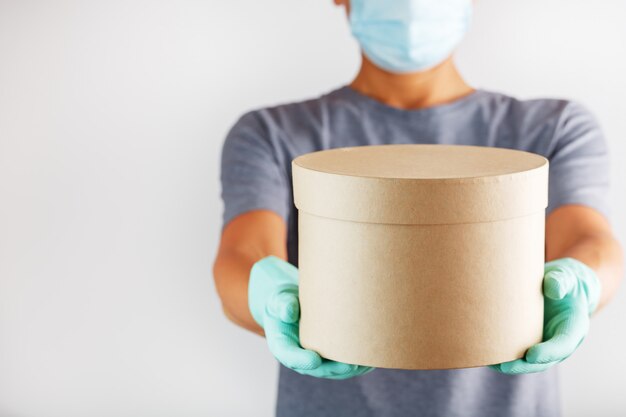 Een bezorger in rubberen handschoenen en een masker houdt het pakket vast.